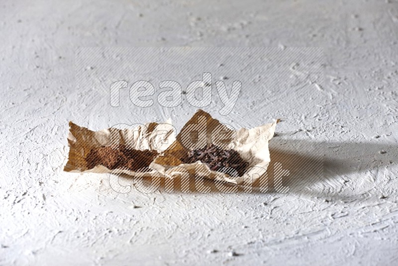 بودرة وحبوب القرنفل في قطعتان من الورق علي خلفية بيضاء