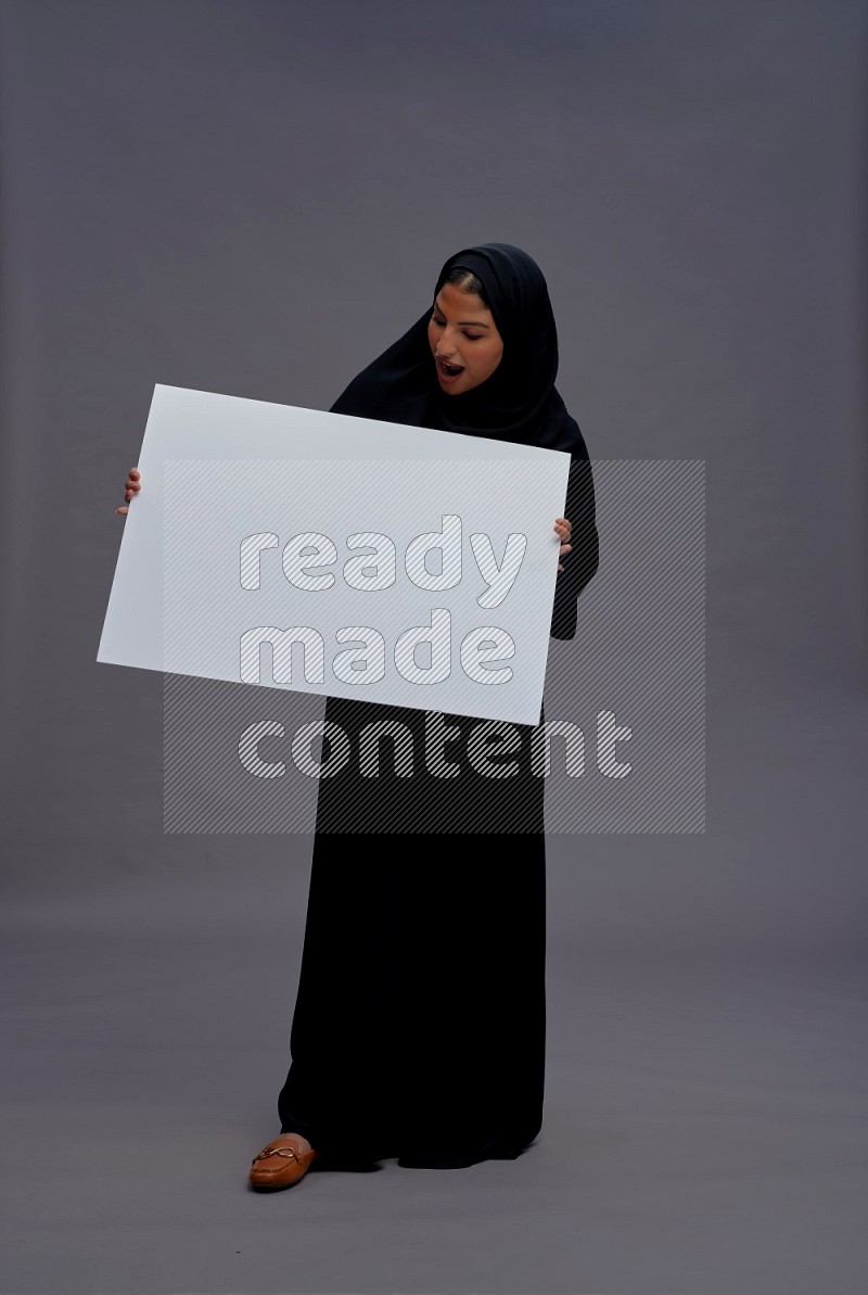 Saudi woman wearing Abaya standing holding white board on gray background