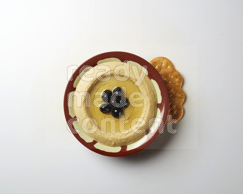 Hummus in a traditional plate garnished with black olives on a white background