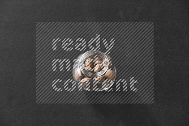 A glass spice jar full of nutmeg on black flooring