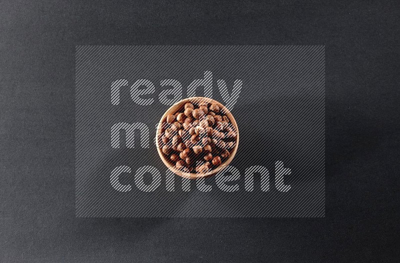 A wooden bowl full of peeled hazelnuts on a black background in different angles