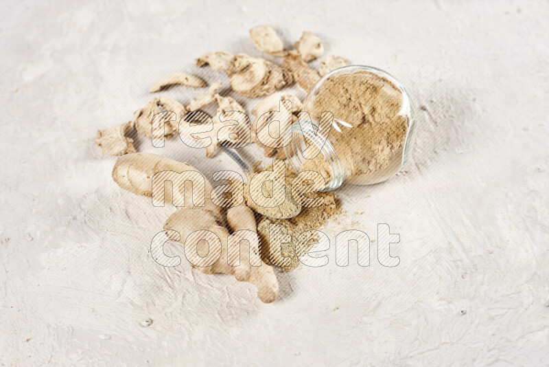 A glass jar full of ground ginger powder flipped with some spilling powder on white background