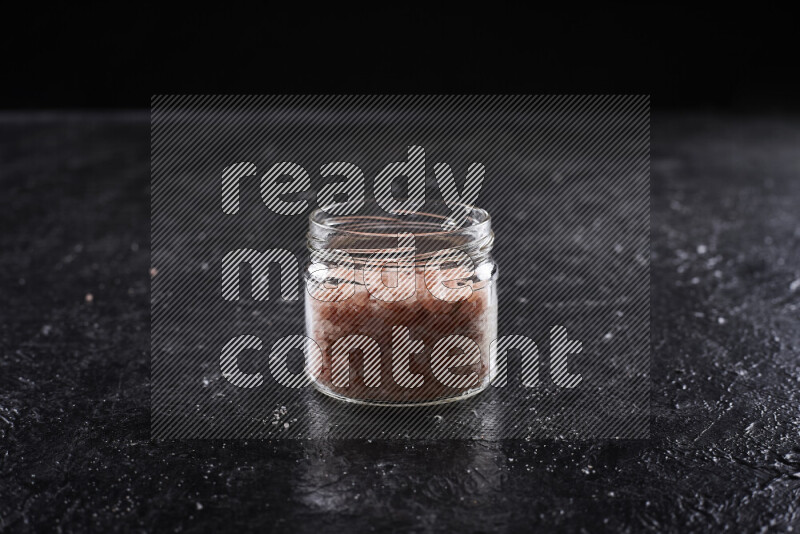 A glass jar full of coarse himalayan salt crystals on black background