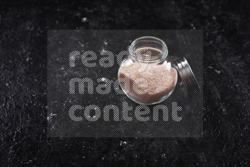 A glass jar full of fine himalayan salt on black background