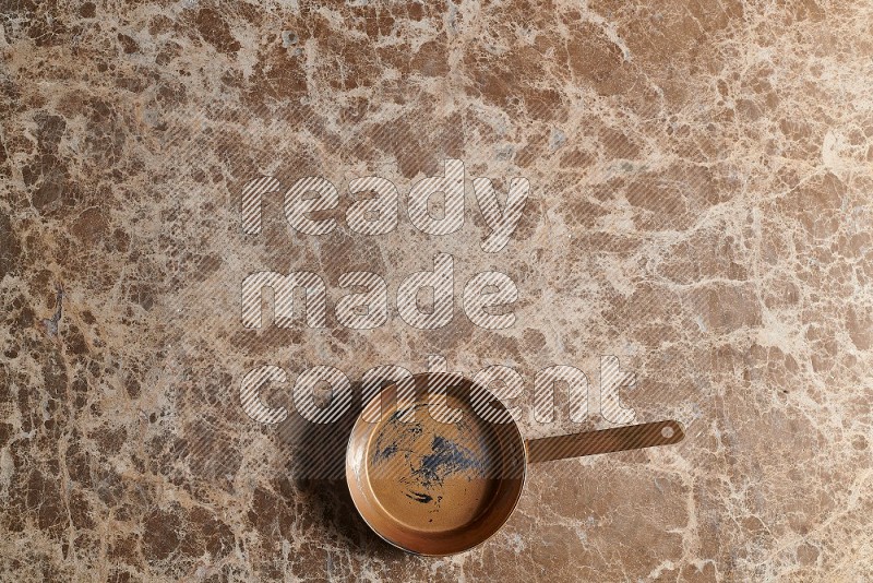 Top View Shot Of A Small Copper pan On beige Marble Flooring