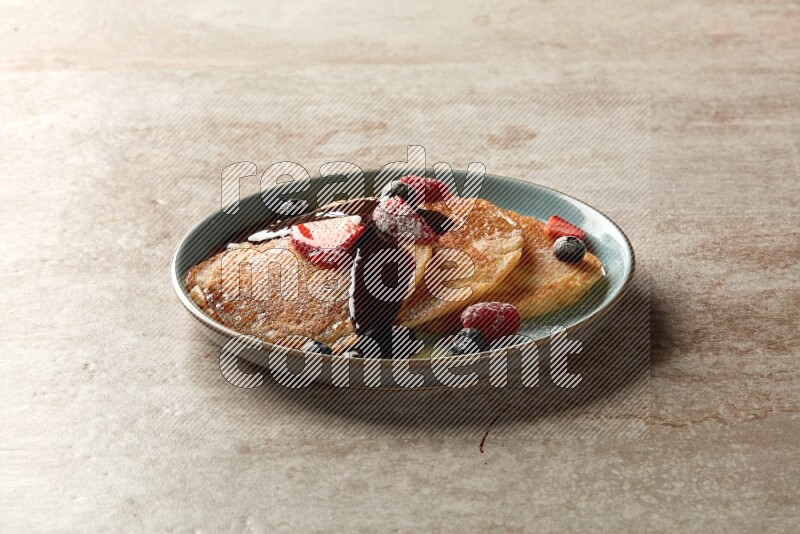 Three stacked mixed berries pancakes in a blue plate on beige background