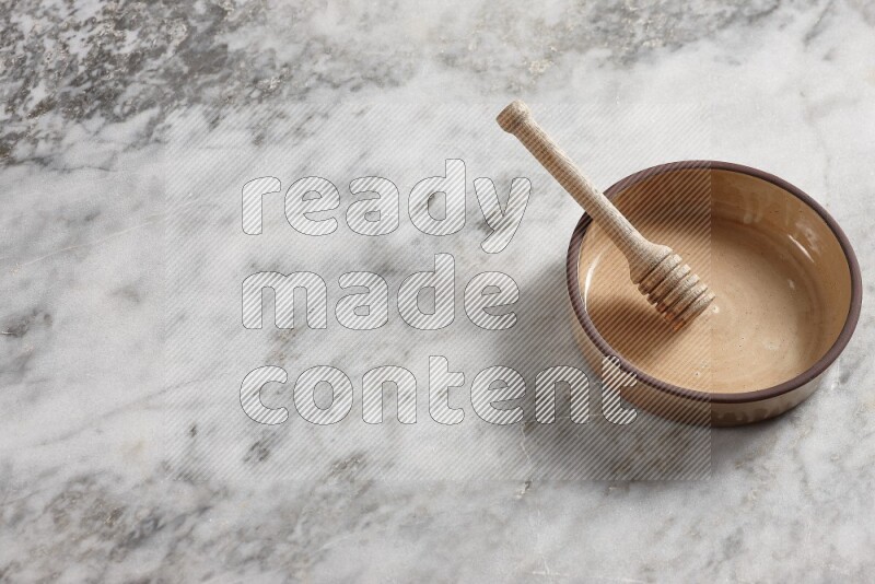 Beige Pottery oven bowl with wooden honey handle on the side with grey marble flooring, 65 degree angle