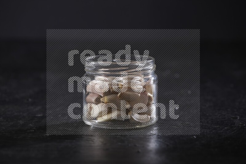 A glass jar full of garlic cloves on a textured black flooring in different angles