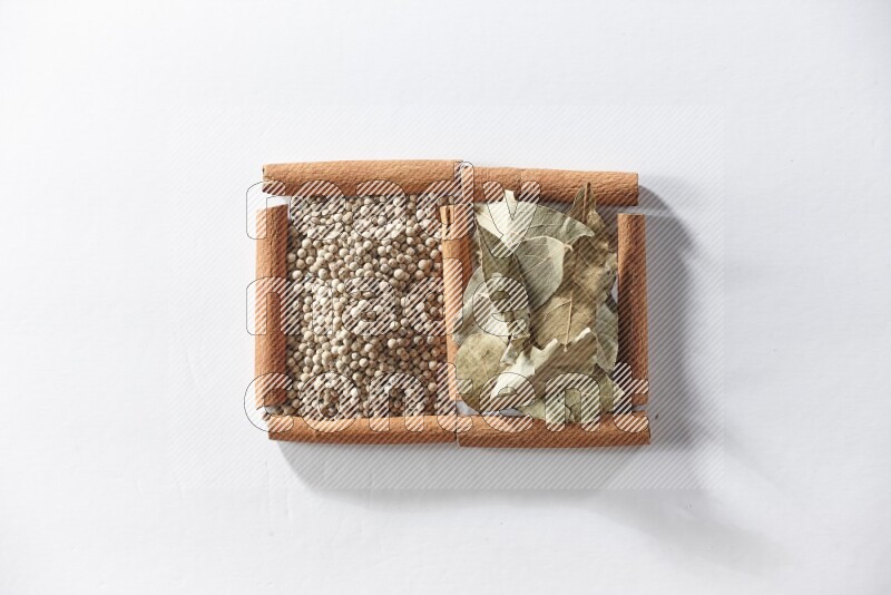 مربعان من أعواد القرفة ممتلئان بحبوب الفلفل الأبيض وأوراق الغار علي خلفية بيضاء