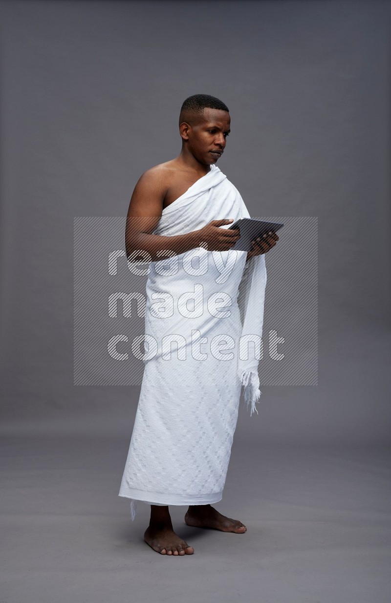 A man wearing Ehram Standing working on tablet on gray background