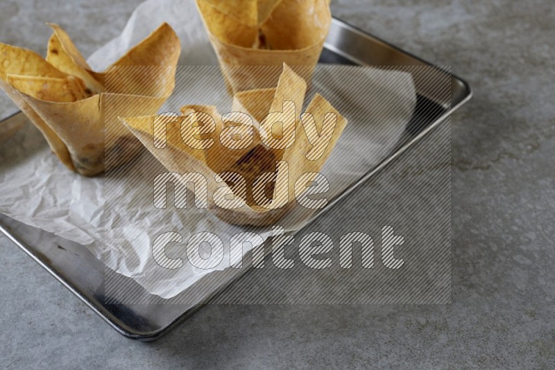 wonton cups on parchment paper in stainless tray on grey textured counter top