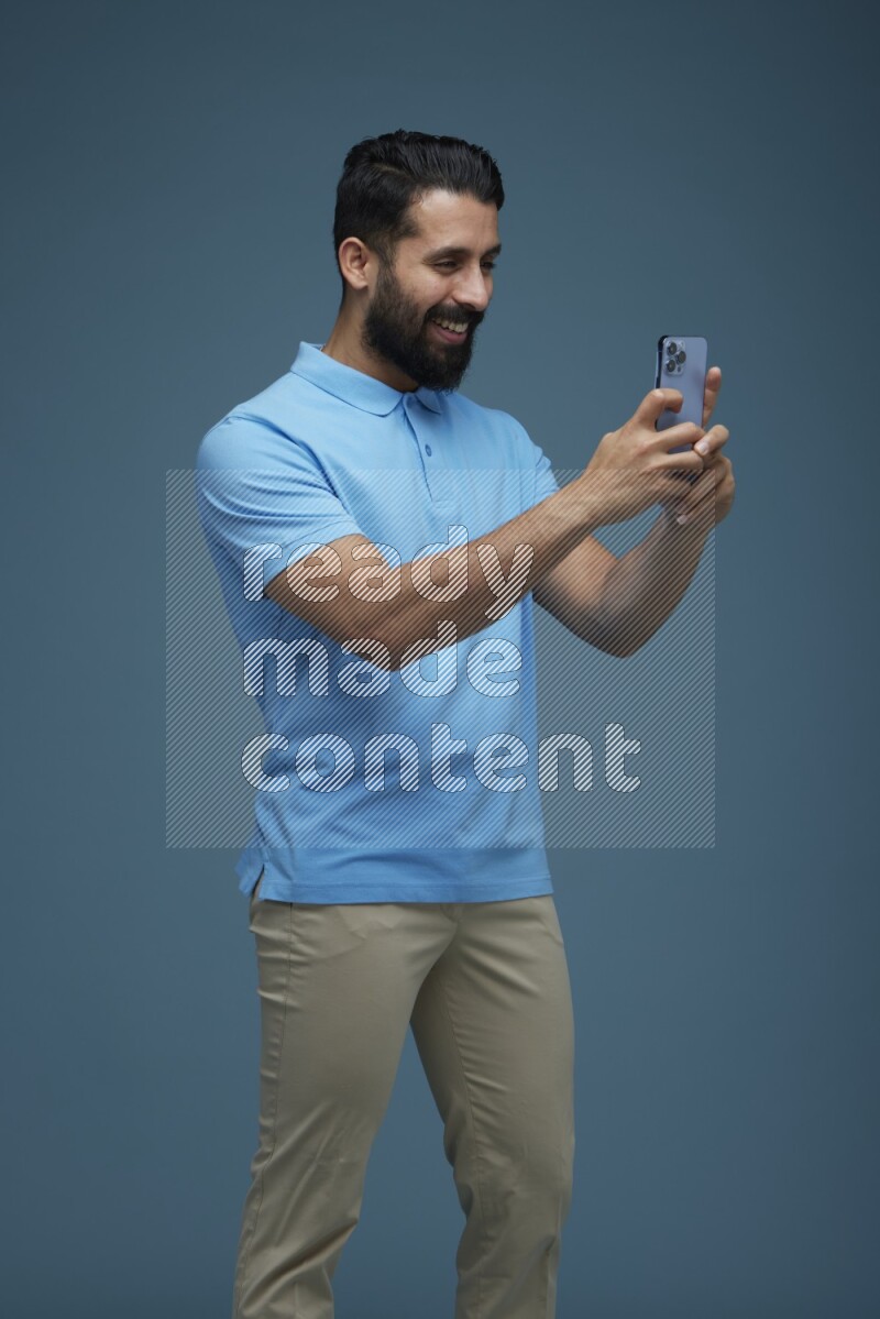 Man taking a picture with his phone  in a blue background wearing a Blue shirt