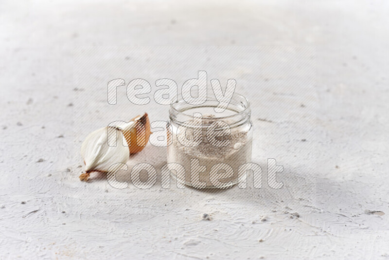 A glass jar full of onion powder on white background