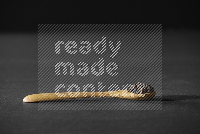 حبوب الفلفل الأسود في ملعقة خشبية علي خلفية سوداء