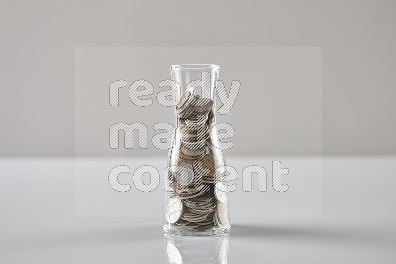 Random old coins in a glass jar on grey background