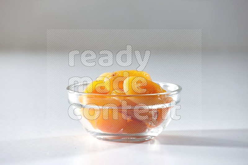 A glass bowl full of dried apricots on a white background in different angles