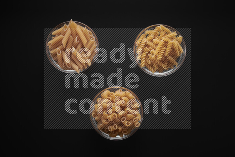 Different pasta types in glass bowls on black background