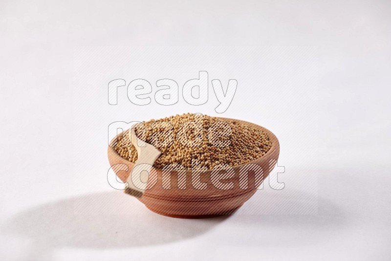 وعاء خشبي ممتلئ ببذور الخردل مع ملعقة خشبية علي البذورعلي خلفية بيضاء