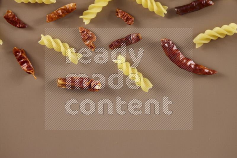 Raw pasta with different ingredients such as cherry tomatoes, garlic, onions, red chilis, black pepper, white pepper, bay laurel leaves, rosemary and cardamom on beige background