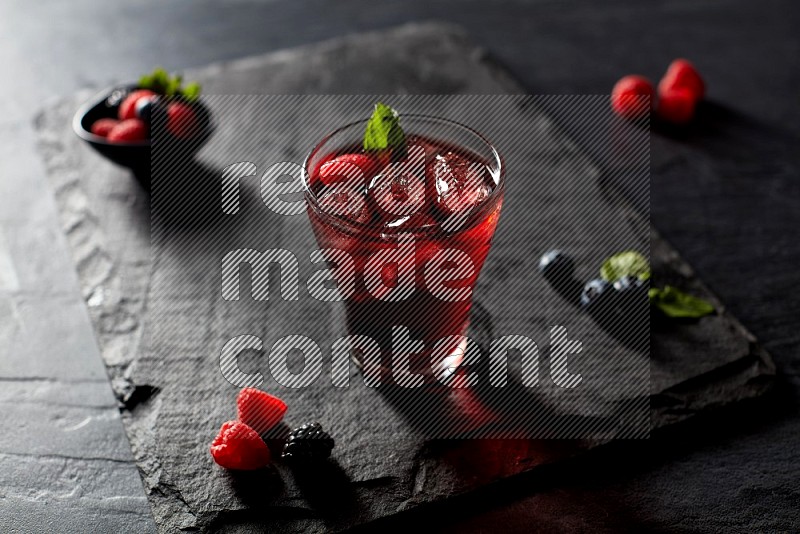 A glass of mixed berries juice with mint leaves on black background