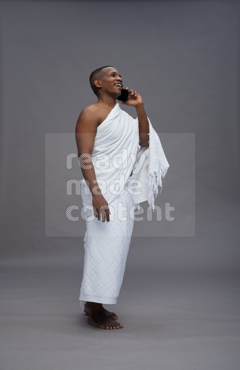 A man wearing Ehram Standing talking on phone on gray background