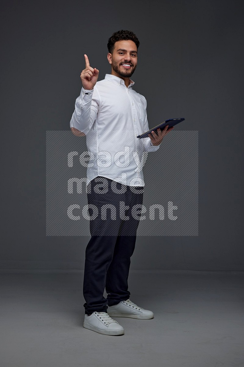 A man wearing smart casual standing and using his tablet and making multi hand gestures eye level on a gray background