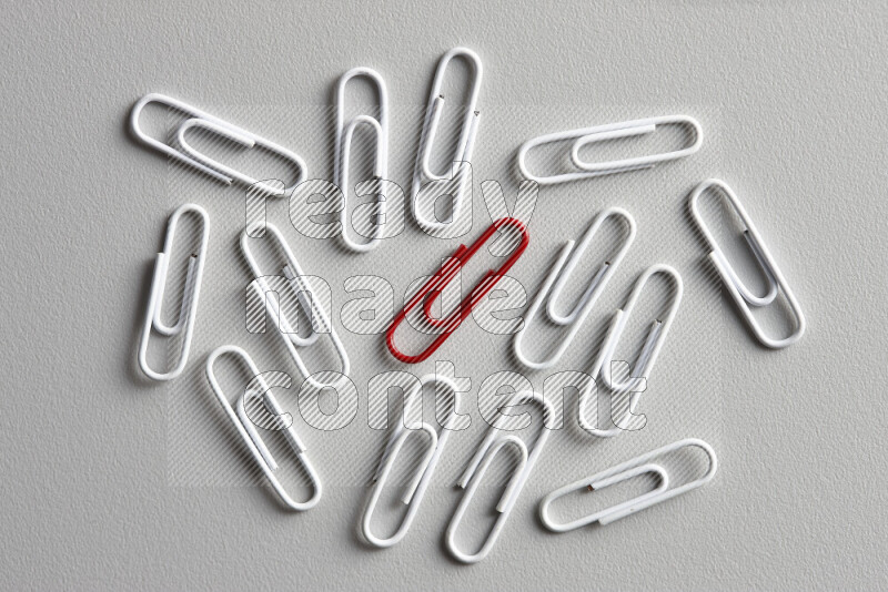 A bunch of white paper clips with a different colored paper clip in the center on grey background
