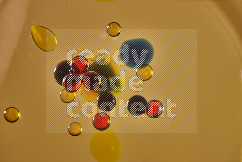 لقطات مقربة لقطرات ألوان مائية حمراء وزرقاء وصفراء على سطح الزيت على خلفية صفراء