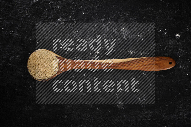 A wooden ladle full of ground ginger powder on black background