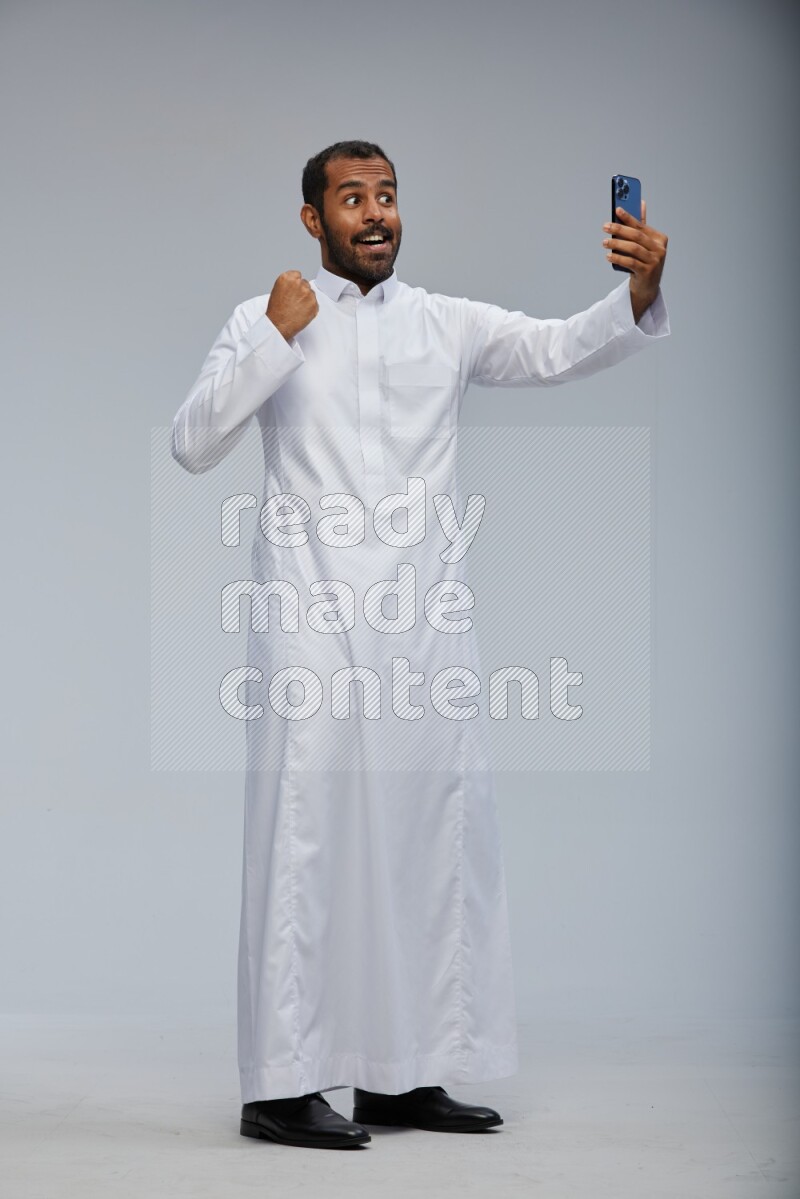 Saudi man wearing Thob standing taking selfie on Gray background