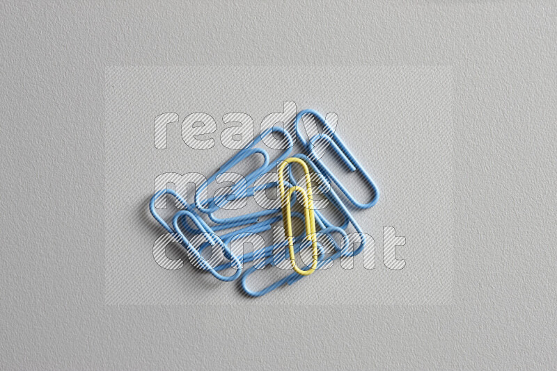 A yellow paperclip surrounded by bunch of blue paperclips on grey background