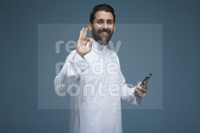 A man posing in a blue background wearing Saudi Thob