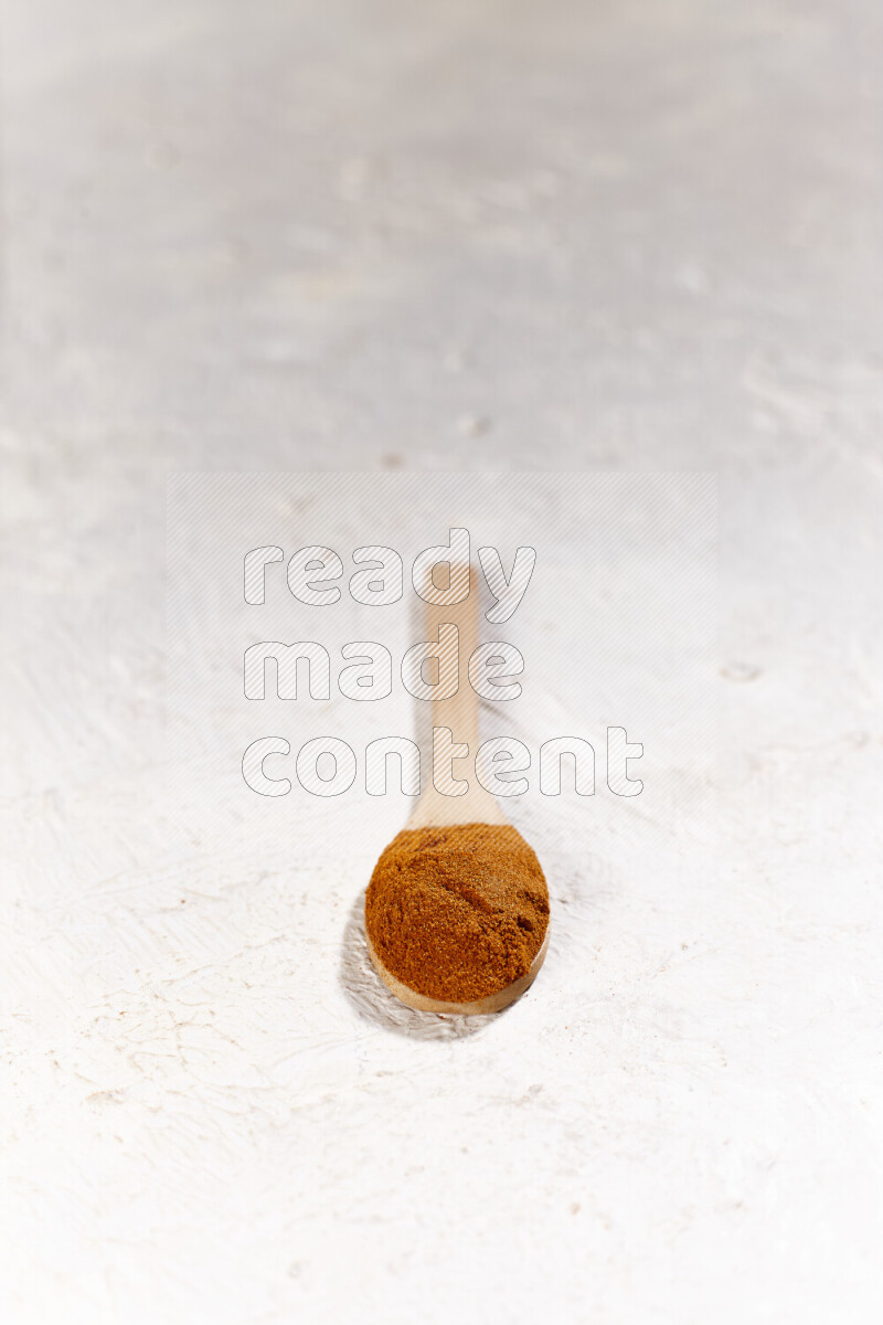 A wooden spoon full of ground paprika powder on white background