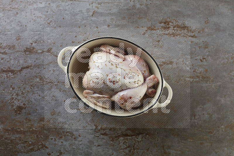 whole raw chicken on in a white ceramic pot direct on a rustic grey background