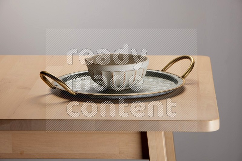off white bowl placed on a rounded stainless steel tray with golden handels on the edge of wooden table