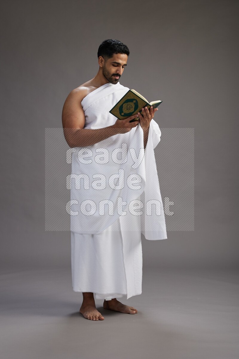 A man wearing Ehram Standing reading quran on gray background