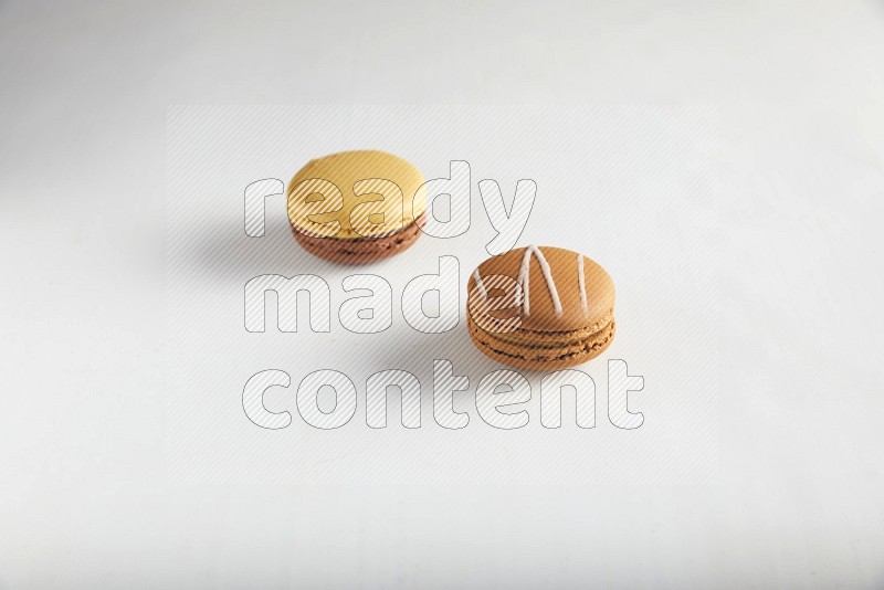 45º Shot of of two assorted Brown Irish Cream, and Yellow, and Brown Chai Latte macarons on white background