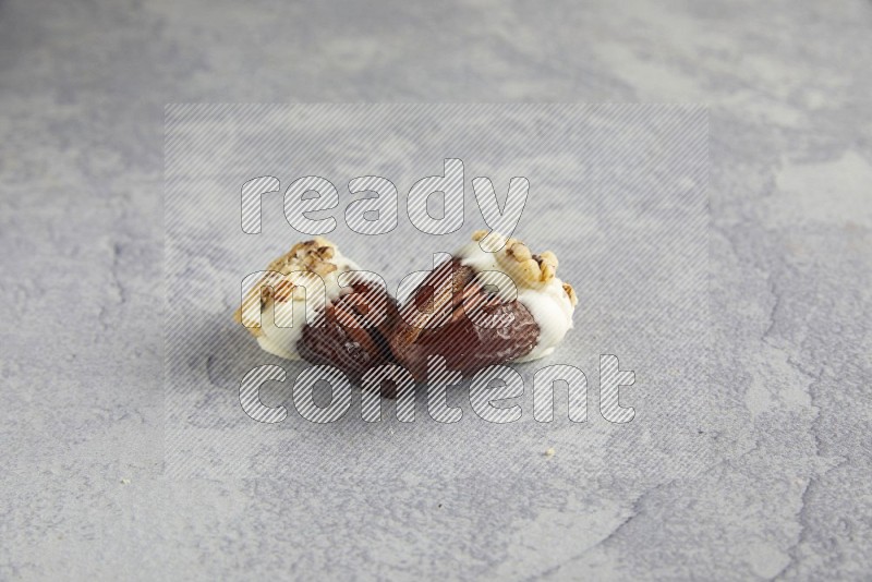 Two pecan stuffed date covered with white chocolate and chopped walnuts on alight grey background