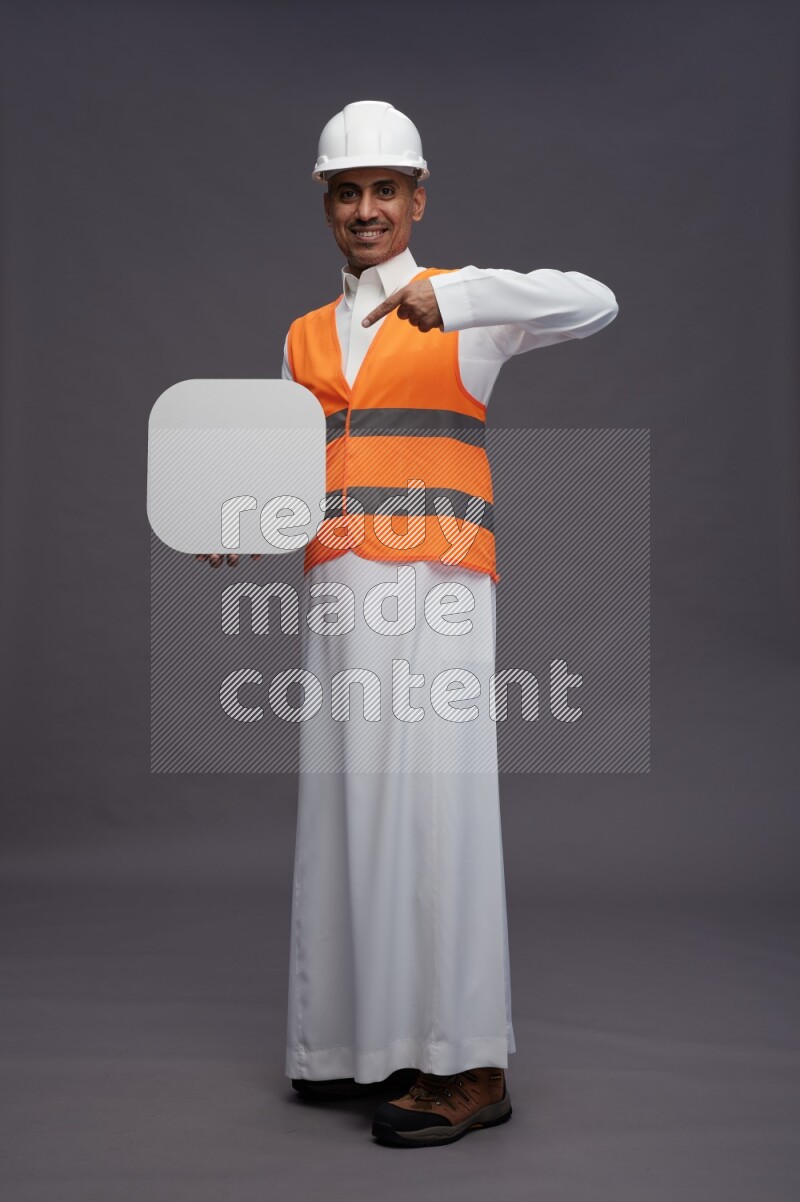Saudi man wearing thob with engineer vest standing holding social media sign on gray background