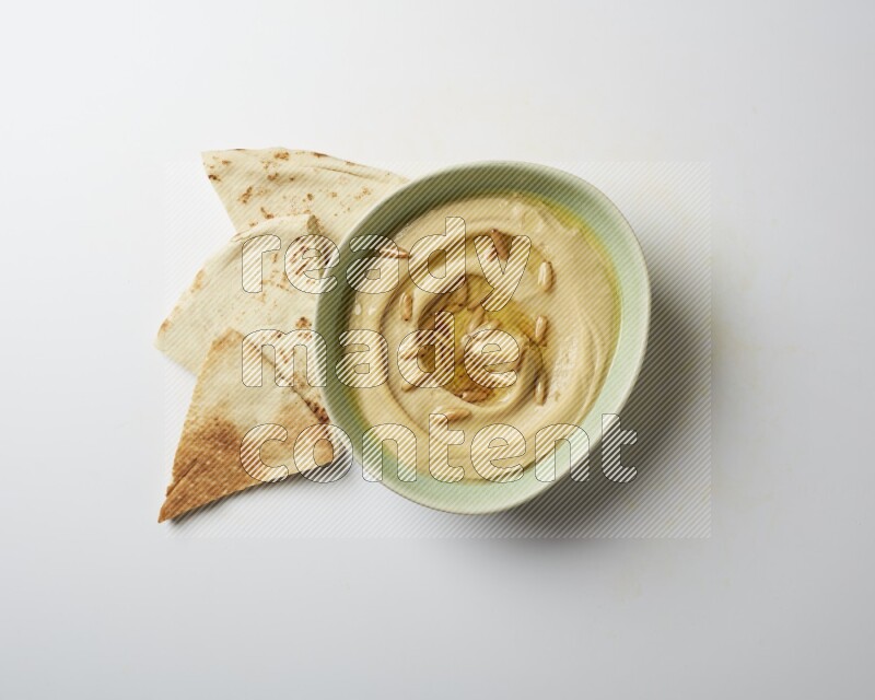 Hummus in a green plate garnished with pine nuts on a white background