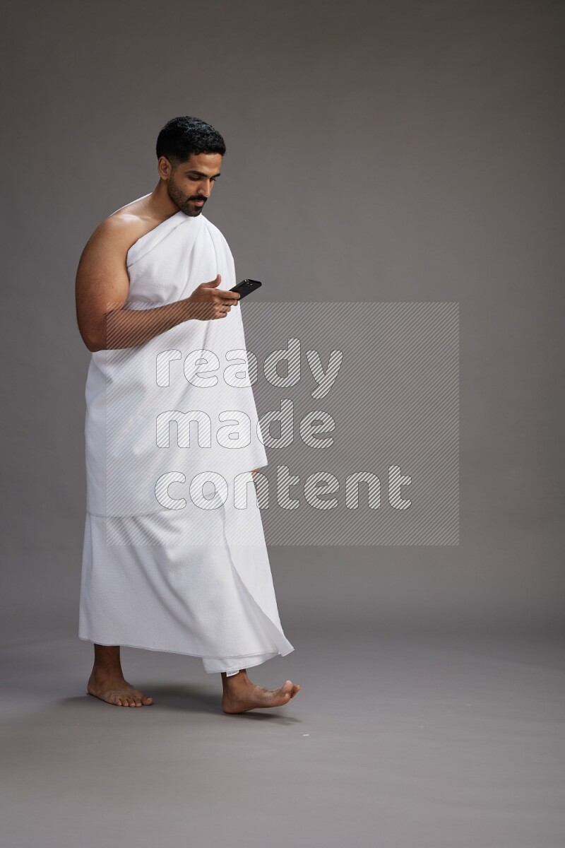 A man wearing Ehram Standing texting on phone on gray background