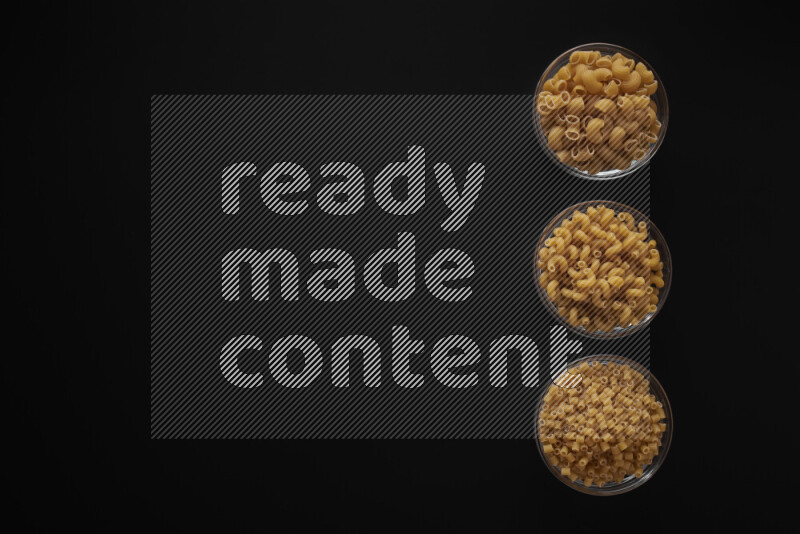 Different pasta types in 3 glass bowls on black background