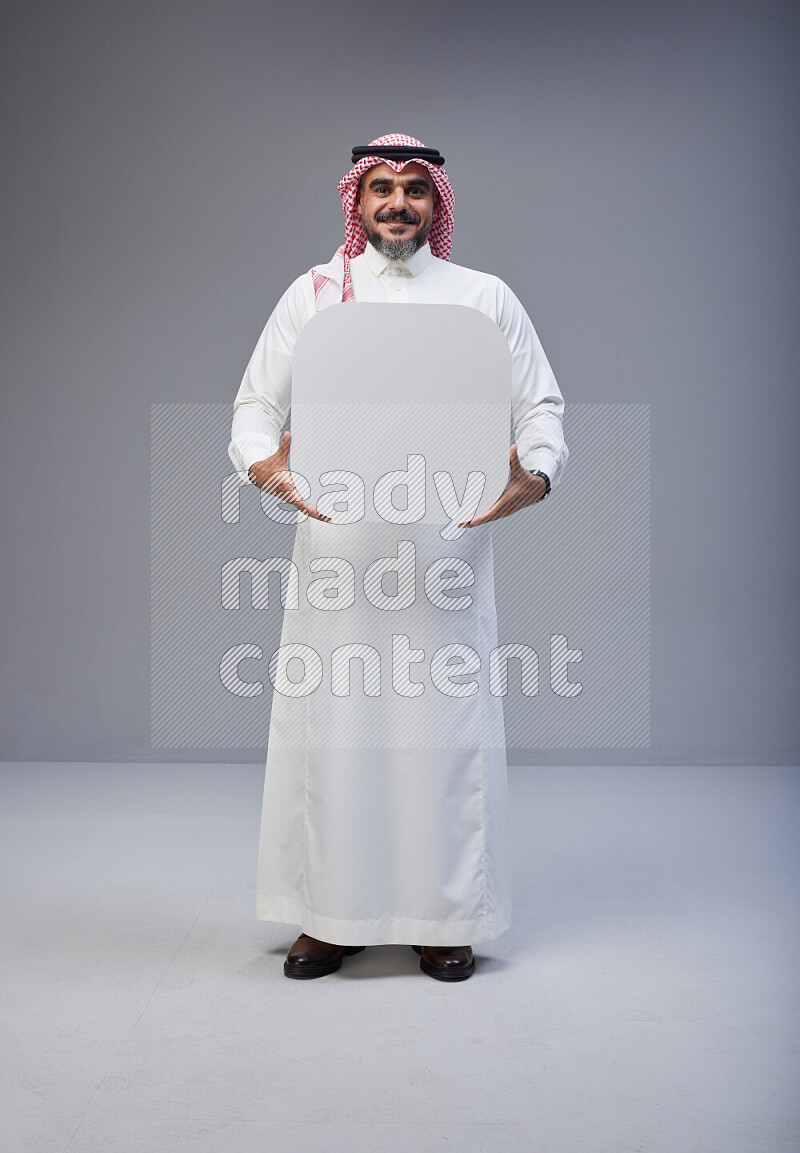 Saudi man Wearing Thob and red Shomag standing holding social media sign on Gray background