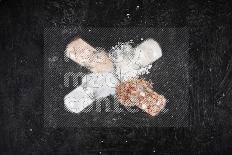 4 glass jars filled with table salt, coarse sea salt, fine himalayan salt and coarse himalayan salt on black background