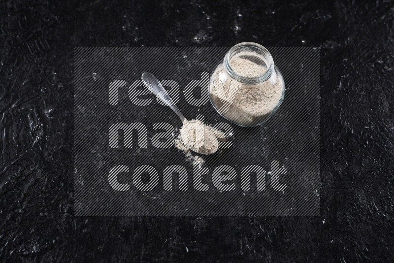 A glass jar full of onion powder on black background