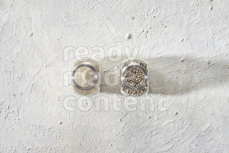 وعاءين زجاجيين عشبيين ممتلئين بحبوب وبودرة الفلفل الأبيض على أرضية بيضاء