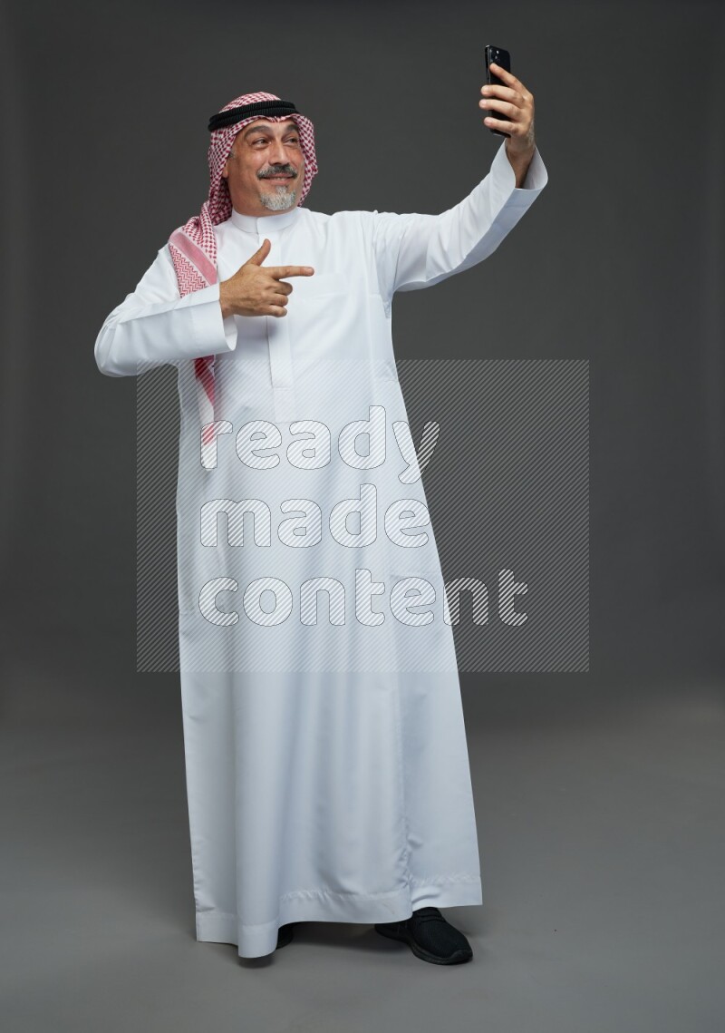 Saudi man with shomag Standing taking selfie on gray background