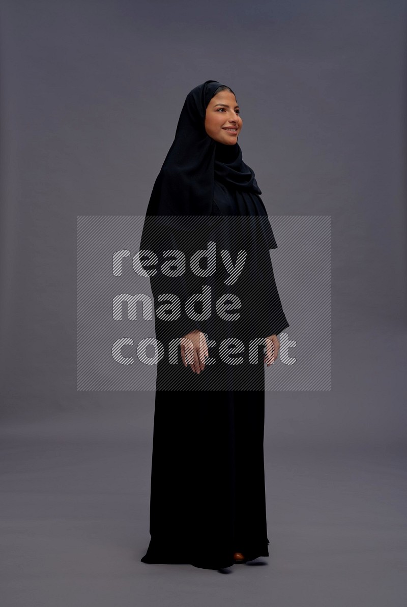 Saudi woman wearing Abaya standing interacting with the camera on gray background