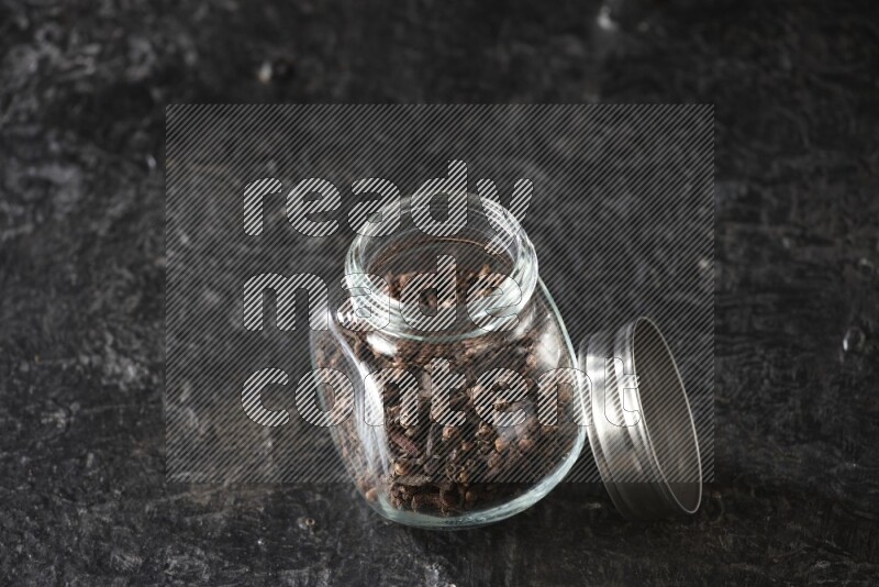 A glass spice jar full of cloves on textured black flooring