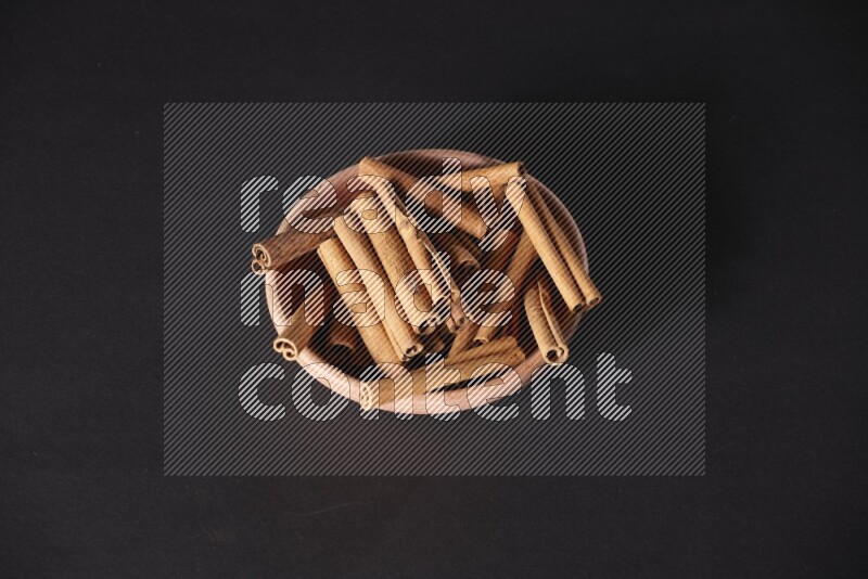 Cinnamon Sticks in a wooden bowl on black background